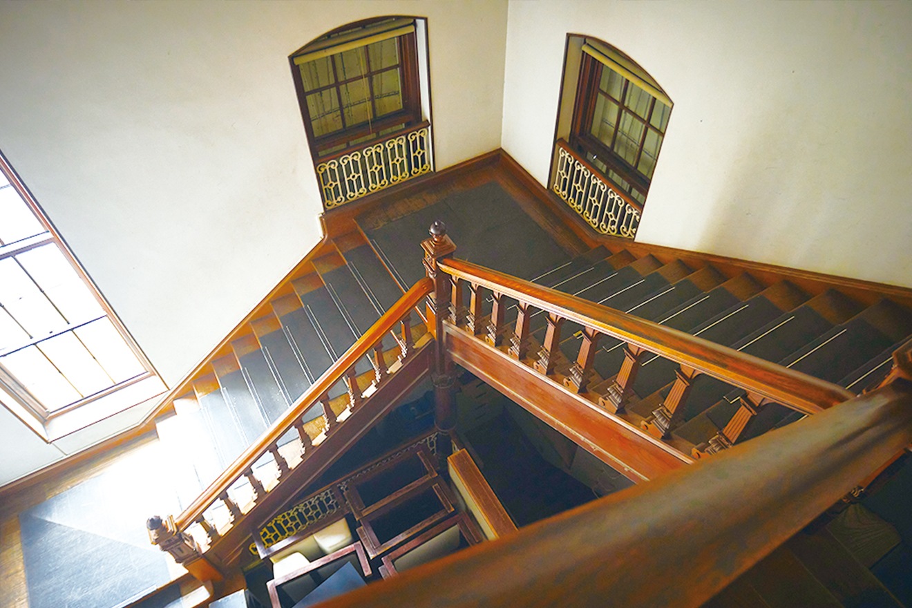 待ち合い室西側の階段は研修室などのあった2階へ繋がっています。装飾彫刻の手すりが使われ、重厚感があります（通常非公開）。