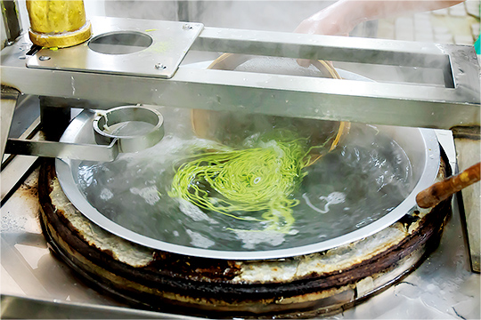 麺状に押し出したすり身を沸騰した釜へ入れ、2 ～3秒のタイミングでサッと引き上げます