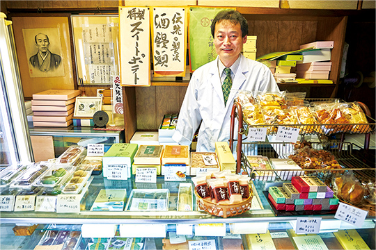 季節の和菓子や銘菓が並ぶ店先に立つ、17代目店主・高岡寛さん